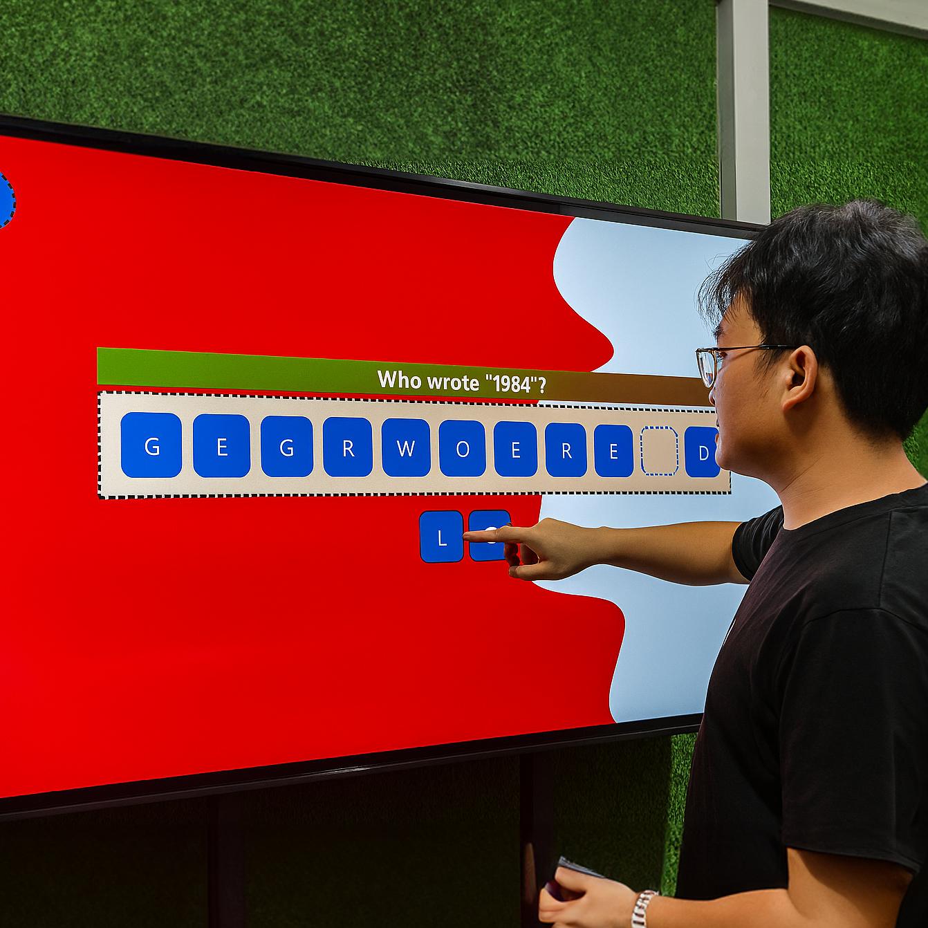 Guest playing word scramble game on large touchscreen at Dubai event with branded graphics and green artificial grass wall background.